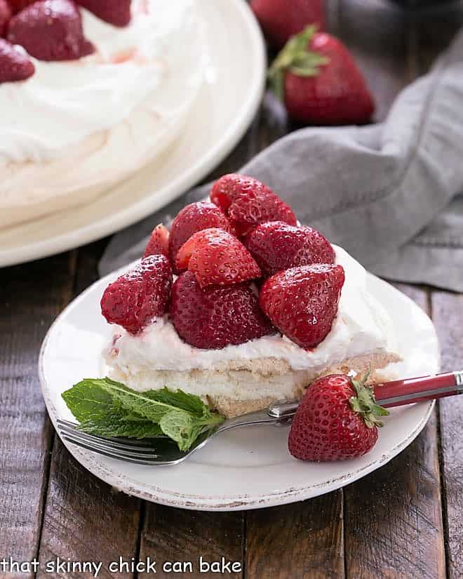 Slice of strawberry pavlova on a dessert plate garnished with fresh mint.