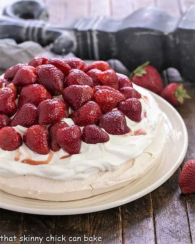 Strawberry Pavlova on a white serving plate topped with halved strawberries and whipped cream.