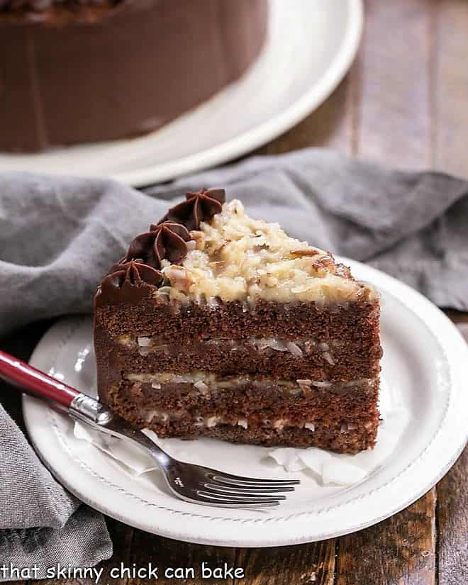 Slice of German Chocolate Cake on a white dessert plate in front of a partial view of the cake