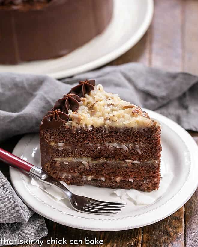 Slice of German Chocolate Cake on a white dessert plate in front of a partial view of the cake.