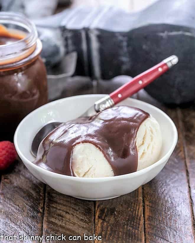 A bowl of vanilla ice cream topped with hot fudge sauce and a red handled spoon
