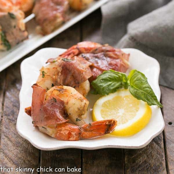 Prosciutto Wrapped Shrimp with Basil Lemon Marinade on a square white plate with a lemon slice and fresh basil.