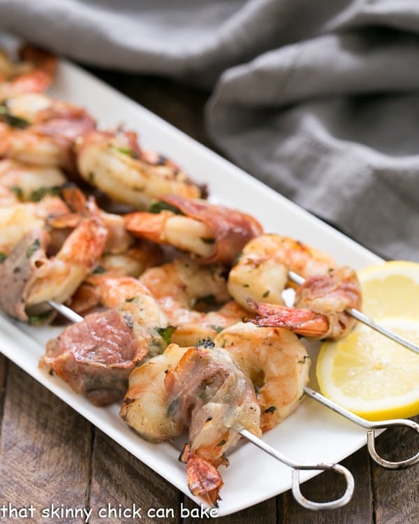 Prosciutto Wrapped Shrimp with Basil Lemon Marinade skewered and lined up on a white platter.