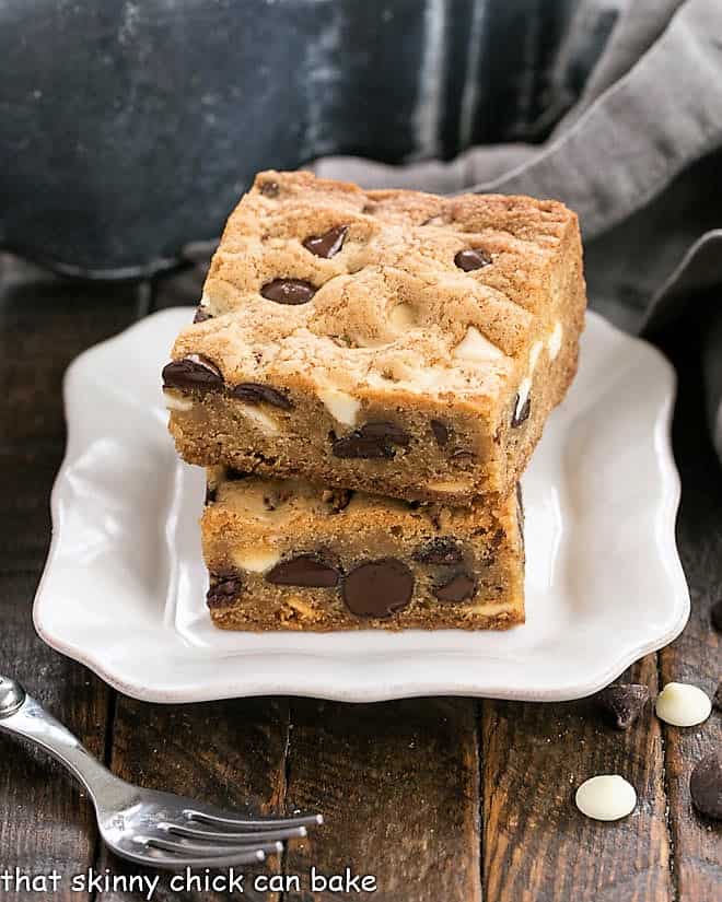 Two chocolate chip bars stacked on a decorative white dessert plate with an adjacent fork.