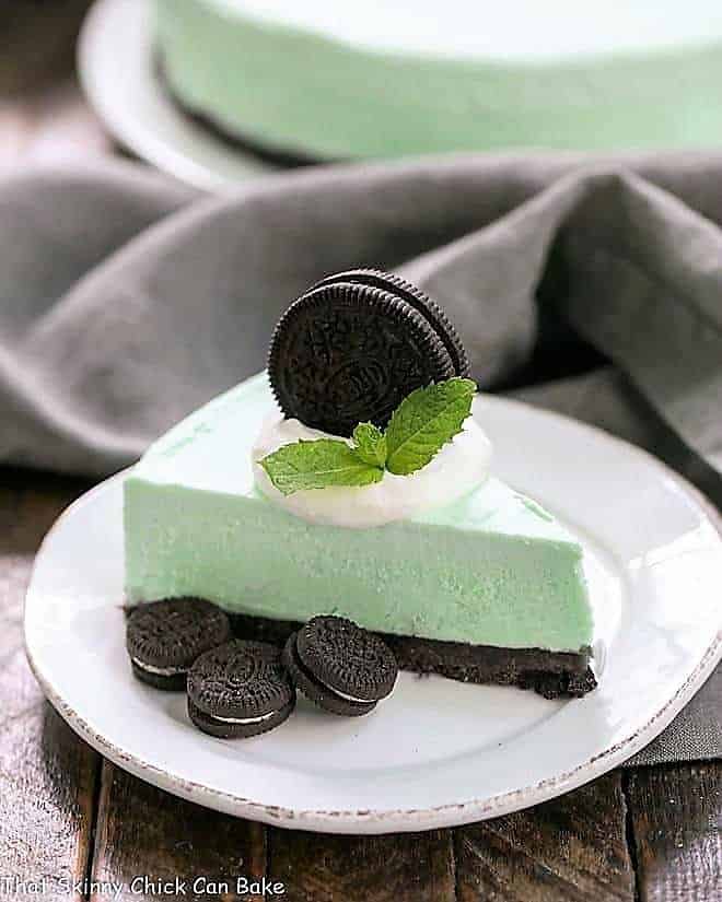 Frozen Grasshopper Pie with an Oreo Crust - Mint lovers will swoon with every bite of this frozen, no bake dessert! Frozen Grasshopper Pie with an Oreo Crust on a small round white plate topped with cream and an Oreo.