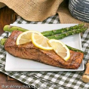 Grilled Asian Salmon garnished with lemon slices and served with asparagus on a square white plate