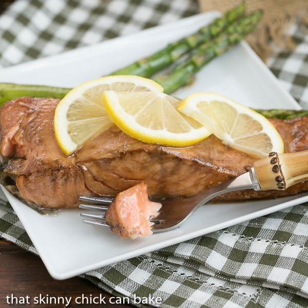 Grilled Asian Salmon bite on a fork along with a serving of salmon garnished with lemon