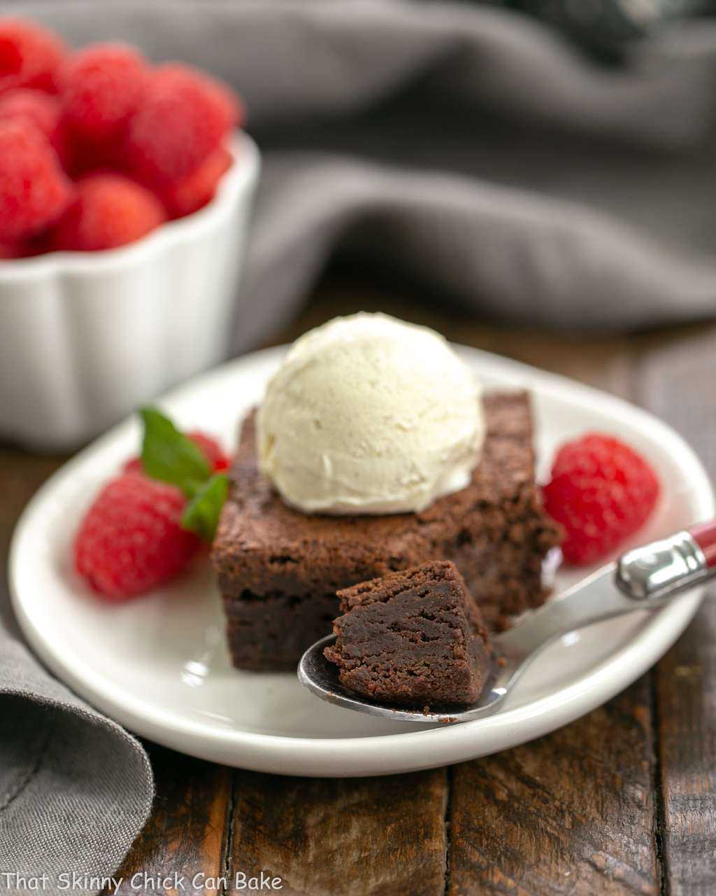 Rich Fudgy Cocoa Brownies on a white plate with a spoon and scoop of vanilla ice cream