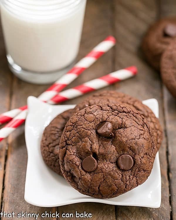 Triple Chocolate Cookies on a square white plate with red and white straws and a glass of milk