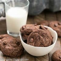 Triple Chocolate Cookies in and around a white bowl with a glass of milk