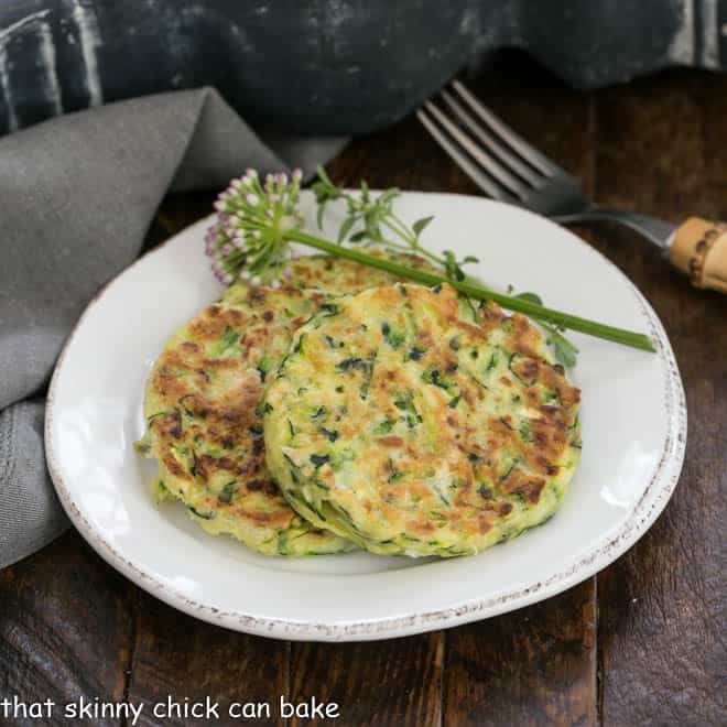 Zucchini fritters on a round white plate with herb garnish