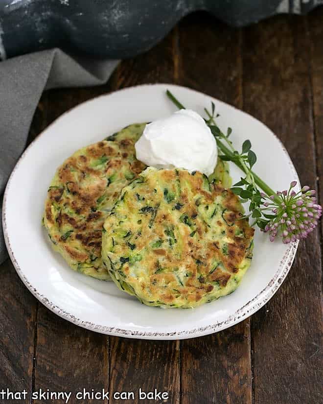 3 Zucchini Fritters on a white plate with herb garnish and sour cream