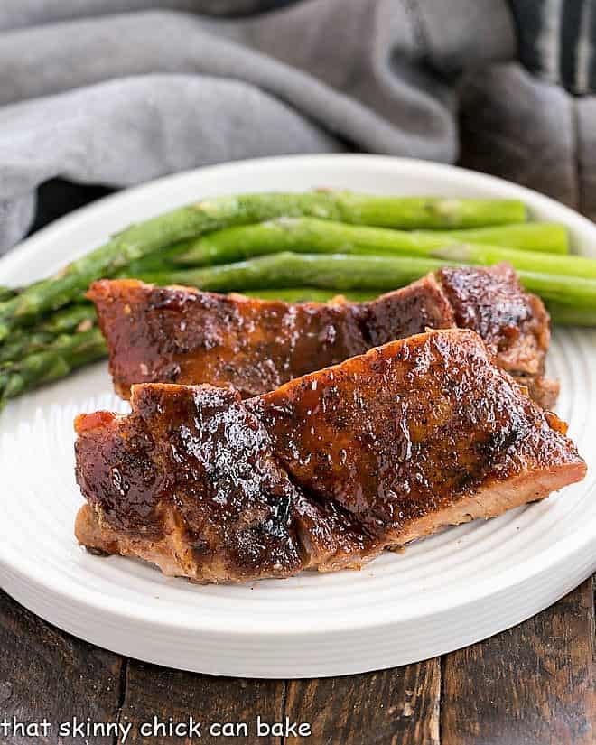 Oven Baked Ribs on a white plate with asparagus spears.