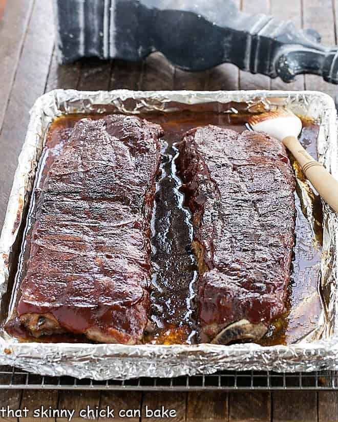 2 racks o baby back ribs on a sheet pan with BBQ sauce applied.