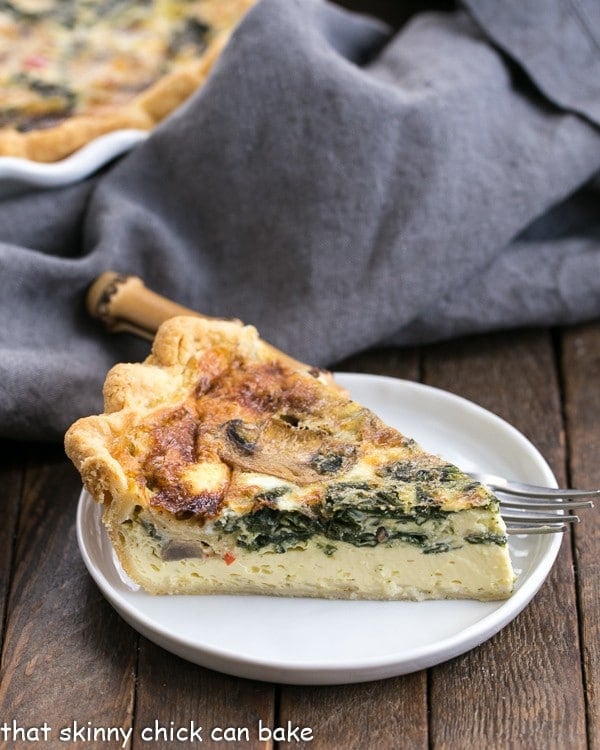 Spinach Mushroom Quiche - A rich, tender quiche full of cheese and vegetables A slice of Spinach Mushroom Quiche on a white plate.