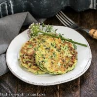 Zucchini fritters on a round white plate with herb garnish