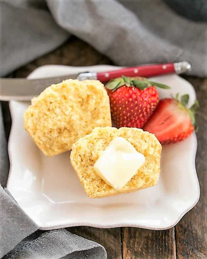 Buttermilk Corn Muffin cut in half with a pat of butter on a square white plate.