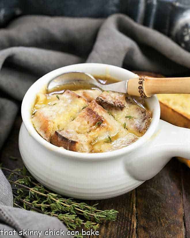 Classic French Onion Soup in a white soup bowl with a bamboo handled spoon.