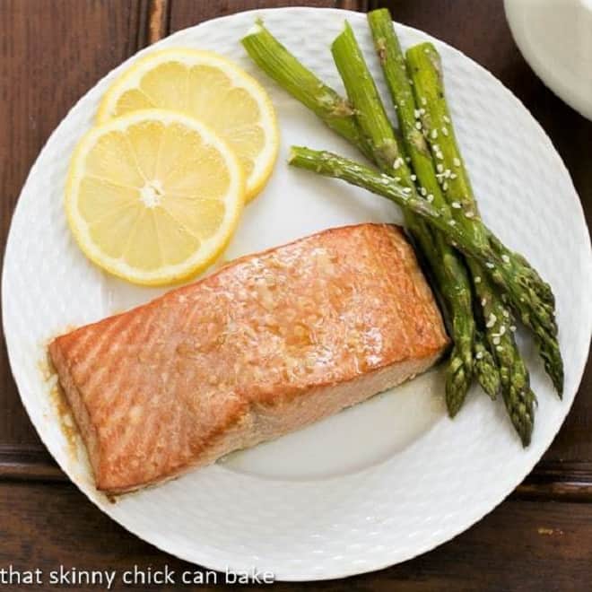 Overhead view of grilled salmon on a white plate with asparagus and lemon slices