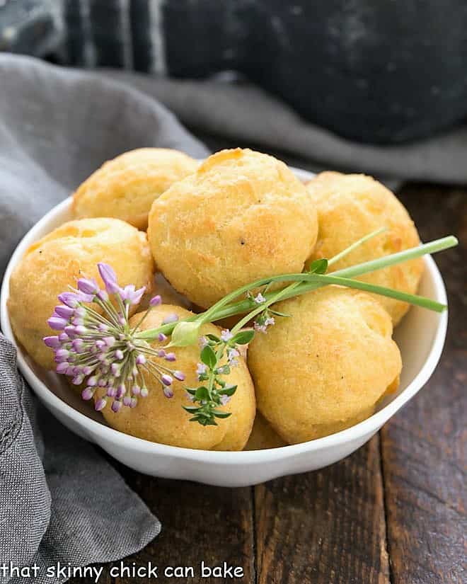 Gougères in a white bowl with herb garnishes.