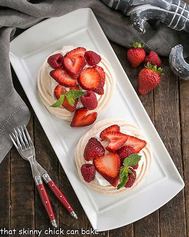 Overhead view of two meringue desserts on a white tray with two red handled forks