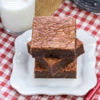 Fat Witch Brownies stacked on a square white plate over a checkered napkin