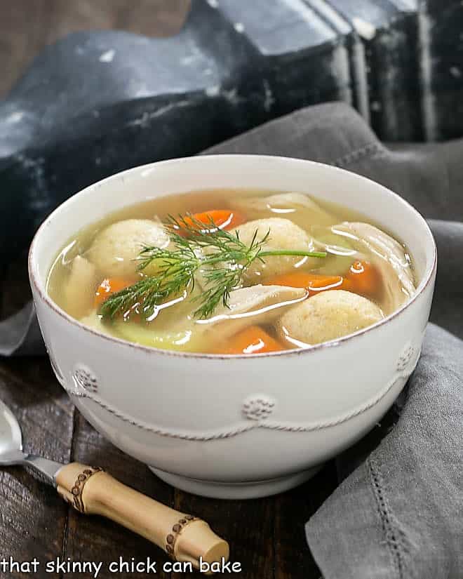 Chicken soup with vegetables topped with a sprig of dill and served with a bamboo spoon.