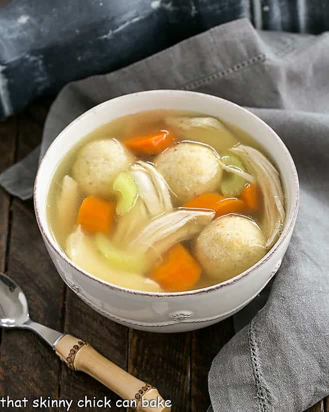 Chicken vegetable soup in a white bowl with a bamboo spoon