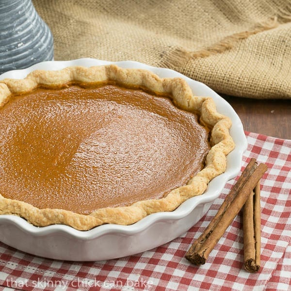 Classic Pumpkin Pie in a white ceramic pie plate on a red and white checked napin.