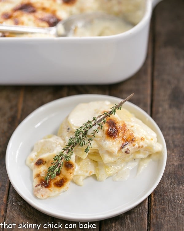 French Potato Gratin topped with a sprig of thyme on a small white dish.
