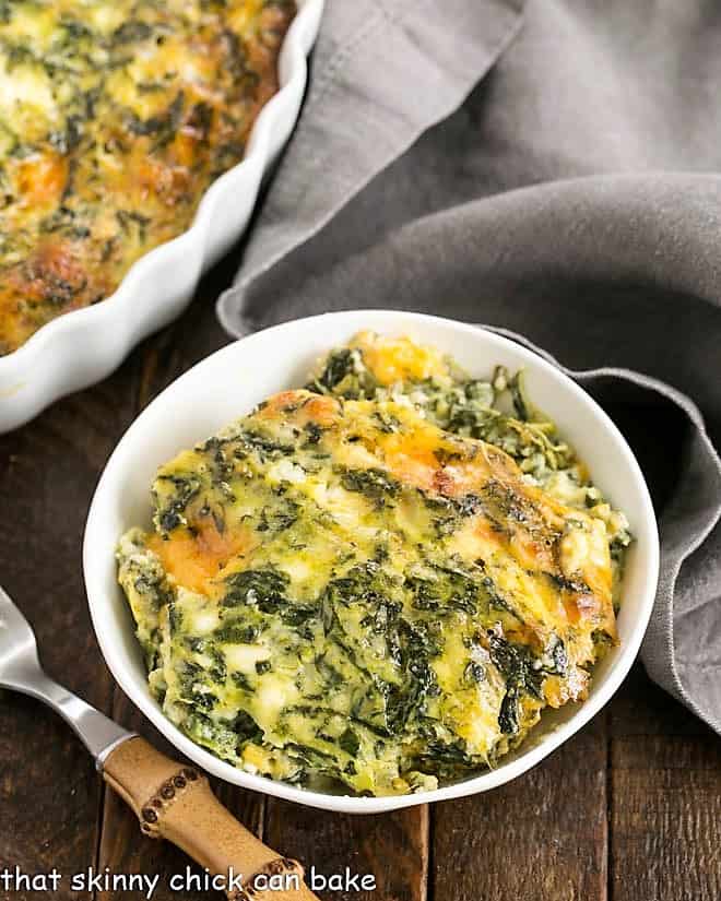 Overhead view of a small white bowl filled with spinach souffle next to a bamboo handle fork.