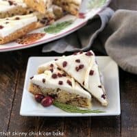 3 cranberry bliss bars on a square white plate with fresh cranberry and cedar garnish