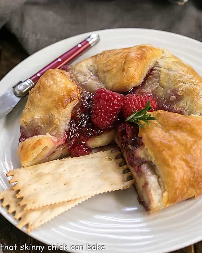 Raspberry Brie en Croute on a serving plate with crackers and a red handled knife