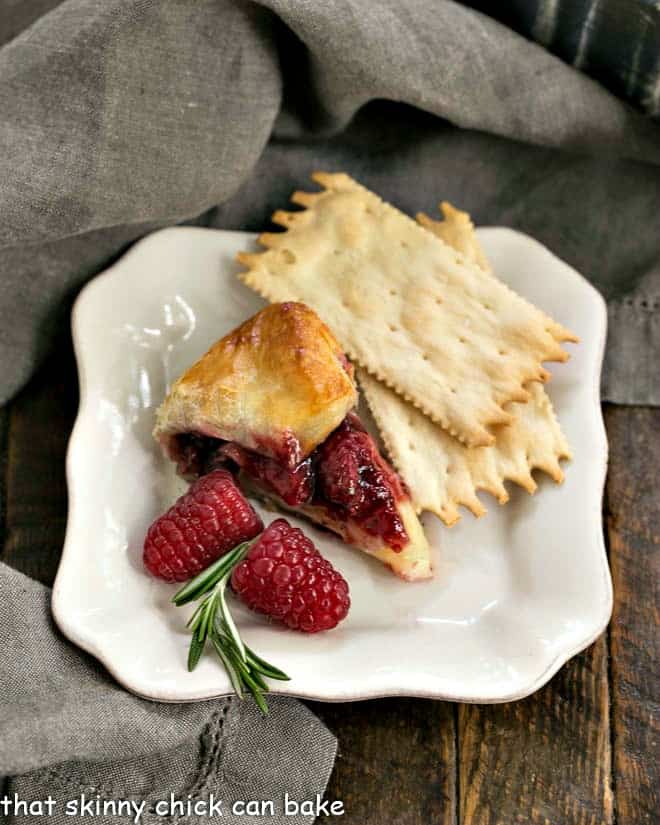 Slice of raspberry brie en croute on an appetizer plate with crackers and fresh raspberries.