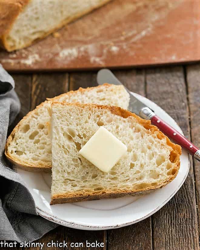 No-Knead Bread - a unique, rustic bread recipe that results in a delicious, rustic loaf with an open crumb Slices of this Easy Bread Recipe with a pat of butter on a small white plate