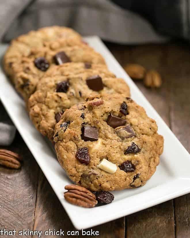 Chewy Oatmeal Cookies with Dark and White Chocolate Chunks, toasted pecans and dried cherries! Perfect for after school snacks, lunch boxes and an after dinner treat! Oatmeal Cookies with Chocolate Chunks, Pecans, and Dried Cherries on a white rectangular tray