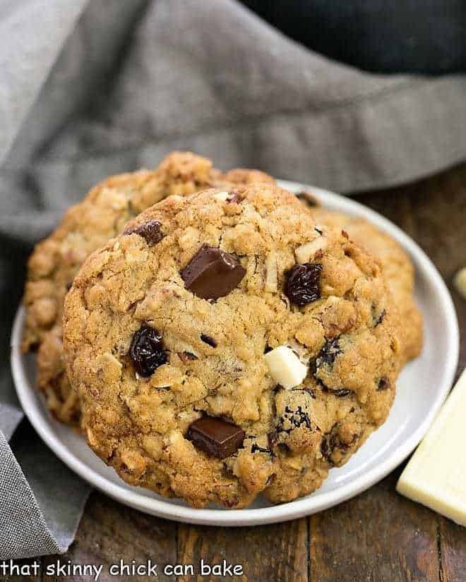 Chewy Oatmeal Cookies with Dark and White Chocolate Chunks, toasted pecans and dried cherries! Perfect for after school snacks, lunch boxes and an after dinner treat! Oatmeal Cookies with Chocolate Chunks, Pecans, and Dried Cherries on a white dessert plate