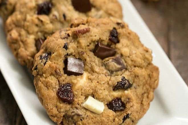 Oatmeal Cookies with Chocolate Chunks, Pecans, and Dried Cherries on a white tray with pecans and cherries
