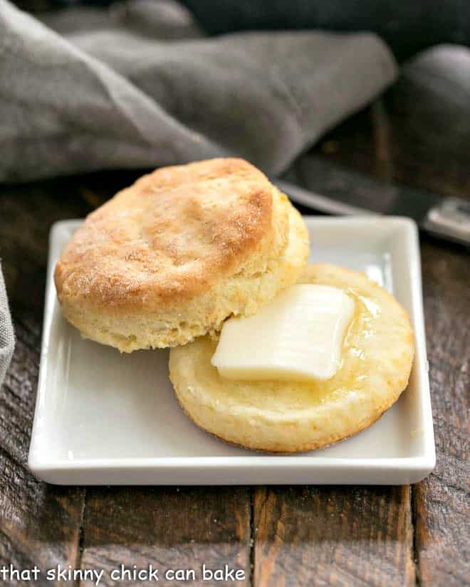 Split buttermilk biscuit with a pat of melting butter on a square white plate