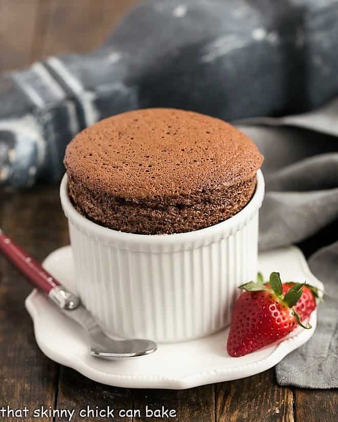 Individual Individual Chocolate Soufflés in ramekins with strawberry garnishes.