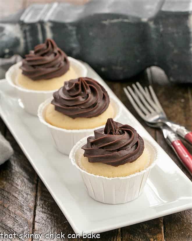 3 boston cream pie cupcakes on a white tray with 2 red handle forks