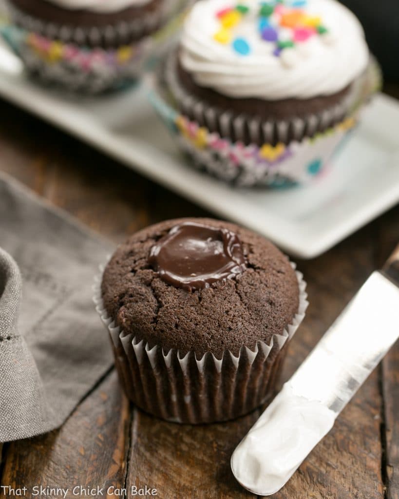 Cocoa Cupcakes with Ganache Filling without frosting with frosted cupcakes in the background.