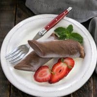 Overhead view of frozen chocolate crepe and berries on a white plate with a red handle fork