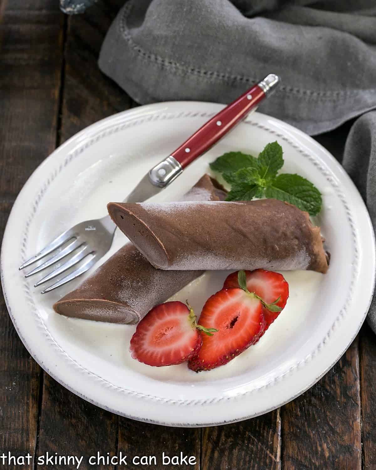 Overhead view of frozen chocolate crepe and berries on a white plate with a red handle fork.