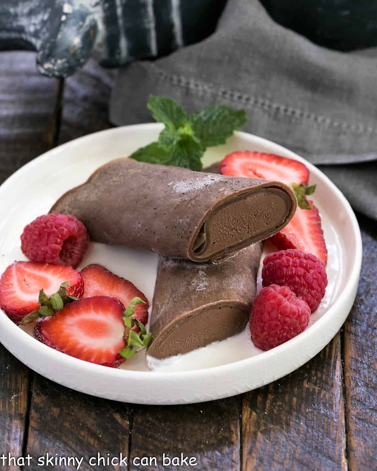 A Frozen chocolate crepe on a rimmed white dessert plate with berries and creme Anglaise.