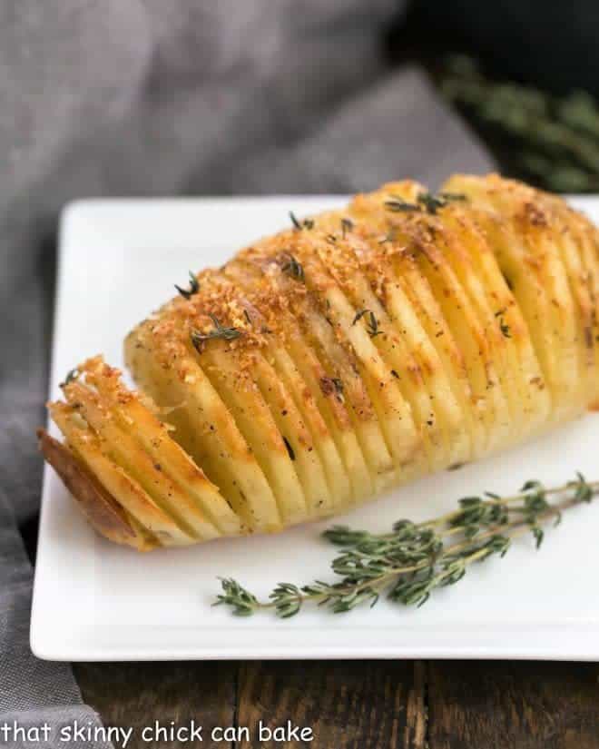 Hasselback Potatoes on a square white plate with a sprig of thyme