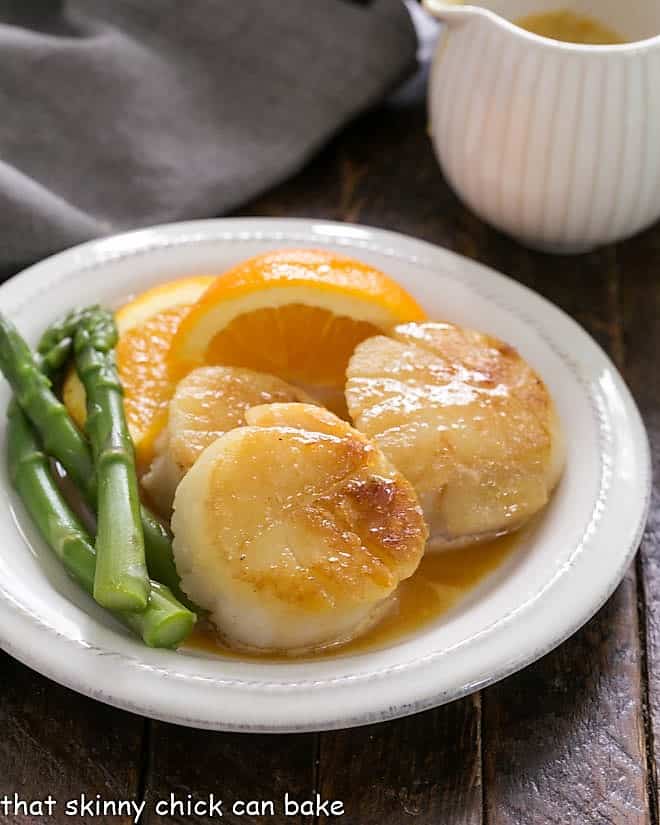 Pan Seared Scallops with Caramel Orange Sauce on a white plate with asparagus