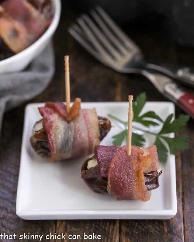 Bacon wrapped dates on a small white appetizer late with red handle forks.
