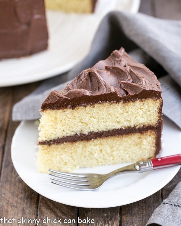 Perfect Yellow Cake Recipe with Chocolate Buttercream - An exquisite, tender yellow cake topped with dreamy chocolate frosting! Slice of Perfect Yellow Cake Recipe with Chocolate Buttercream on a white cake with a red handled fork