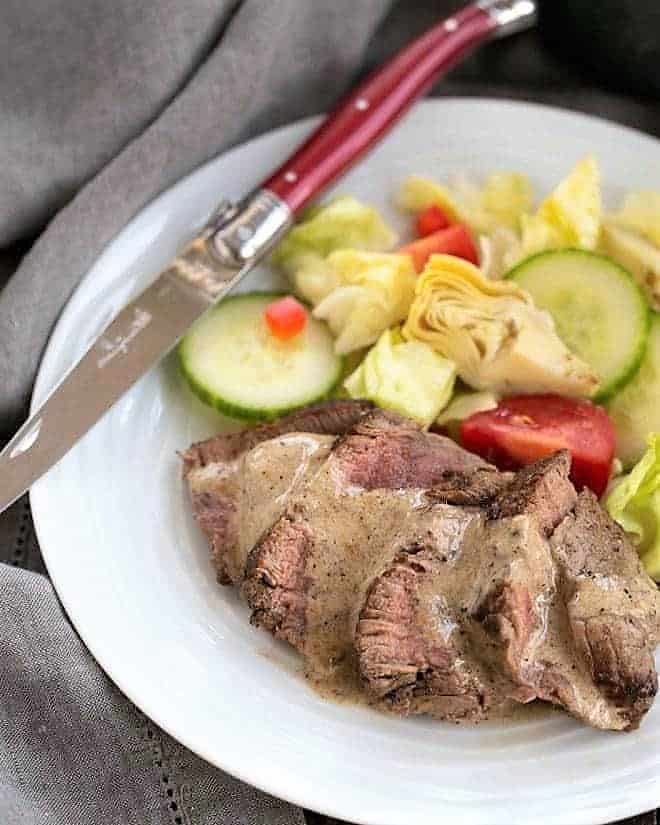 Bistrot Paul Bert Pepper Steak sliced and drizzle with pan sauce with a green salad on a white plate